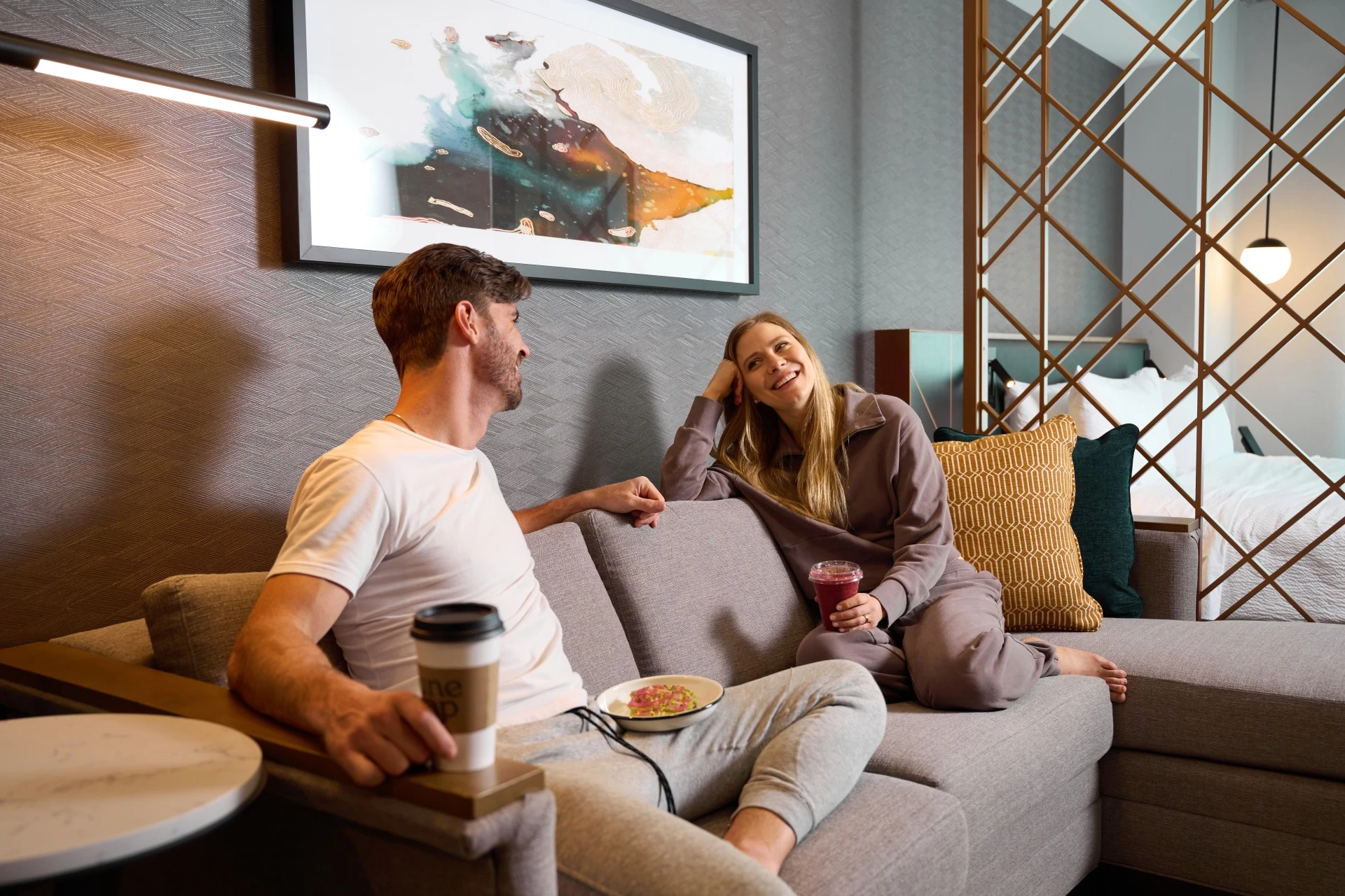 a man and woman sitting on a couch in an Apiary Hotel guest room