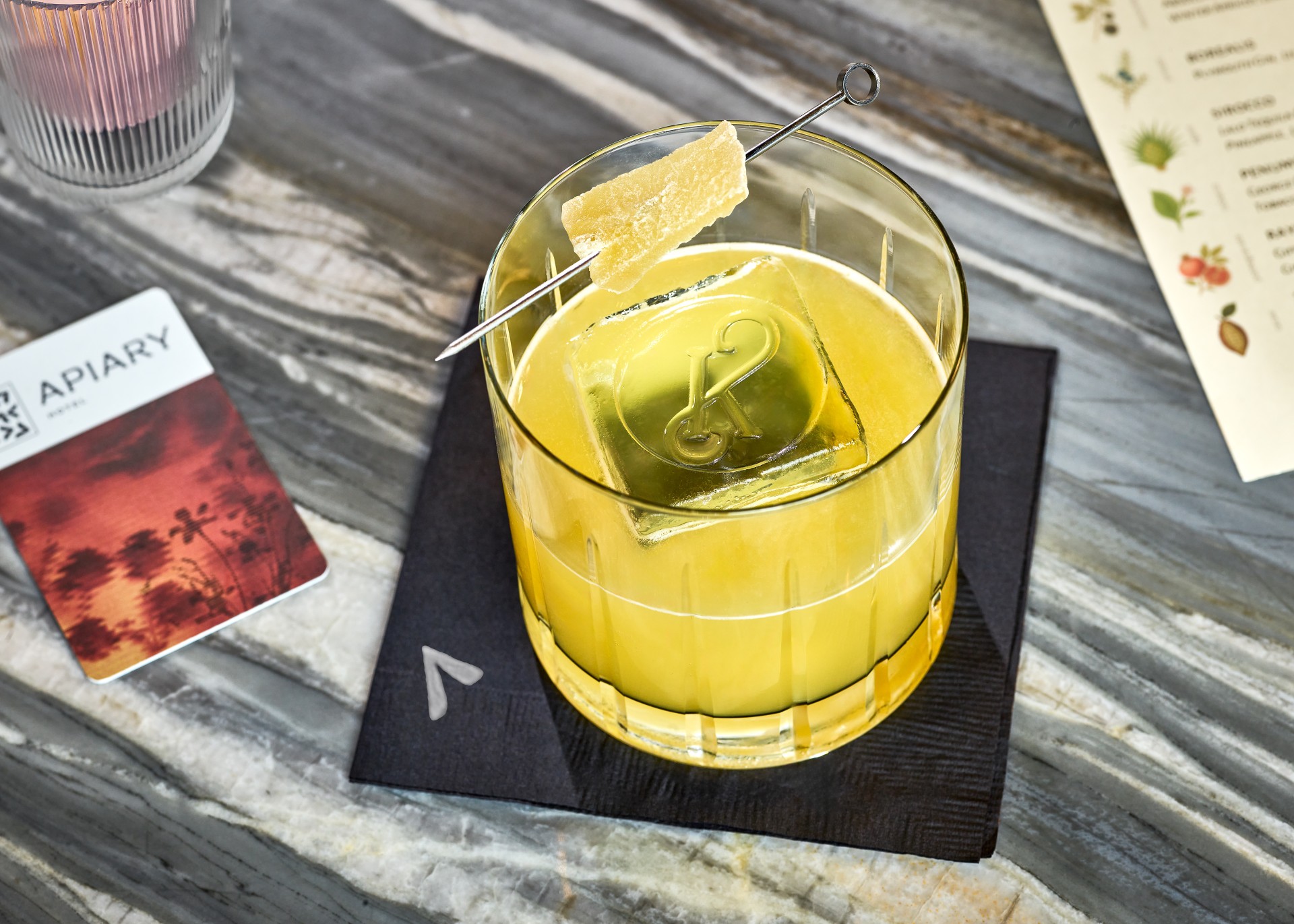 a glass with yellow liquid and a stick on it