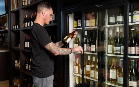 a man opening a glass door with bottles of wine