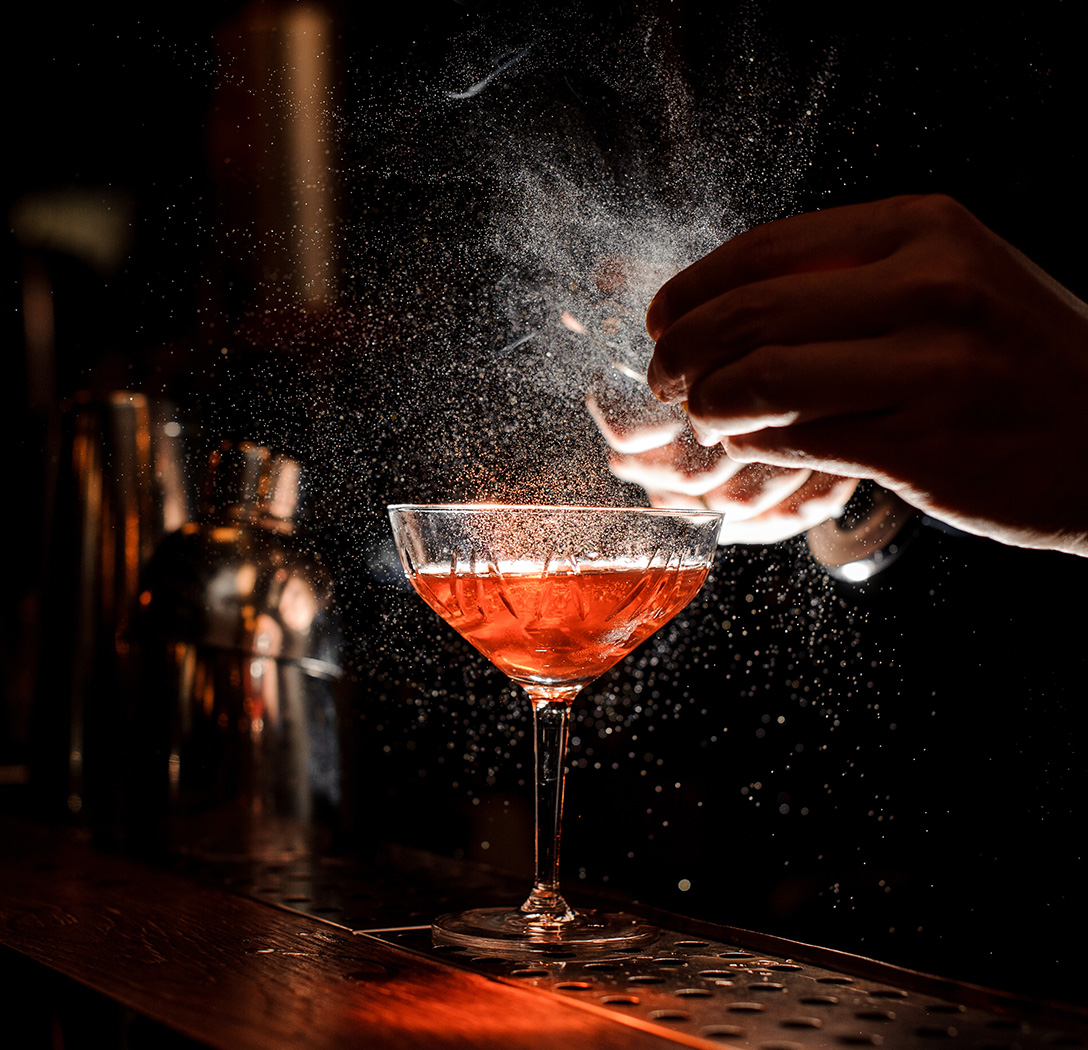 a person sprinkling a drink into a glass