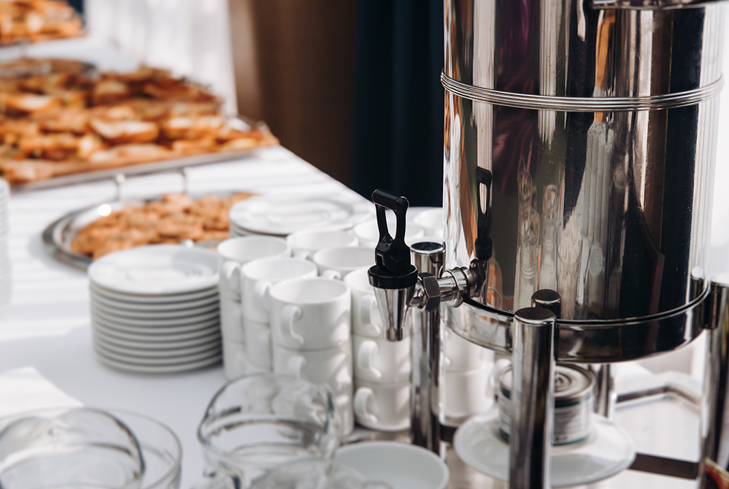 a silver container with a handle on a table with plates and cups