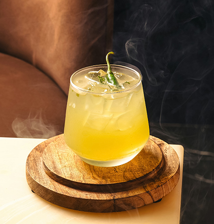 a glass of yellow liquid with a green leaf on top of it