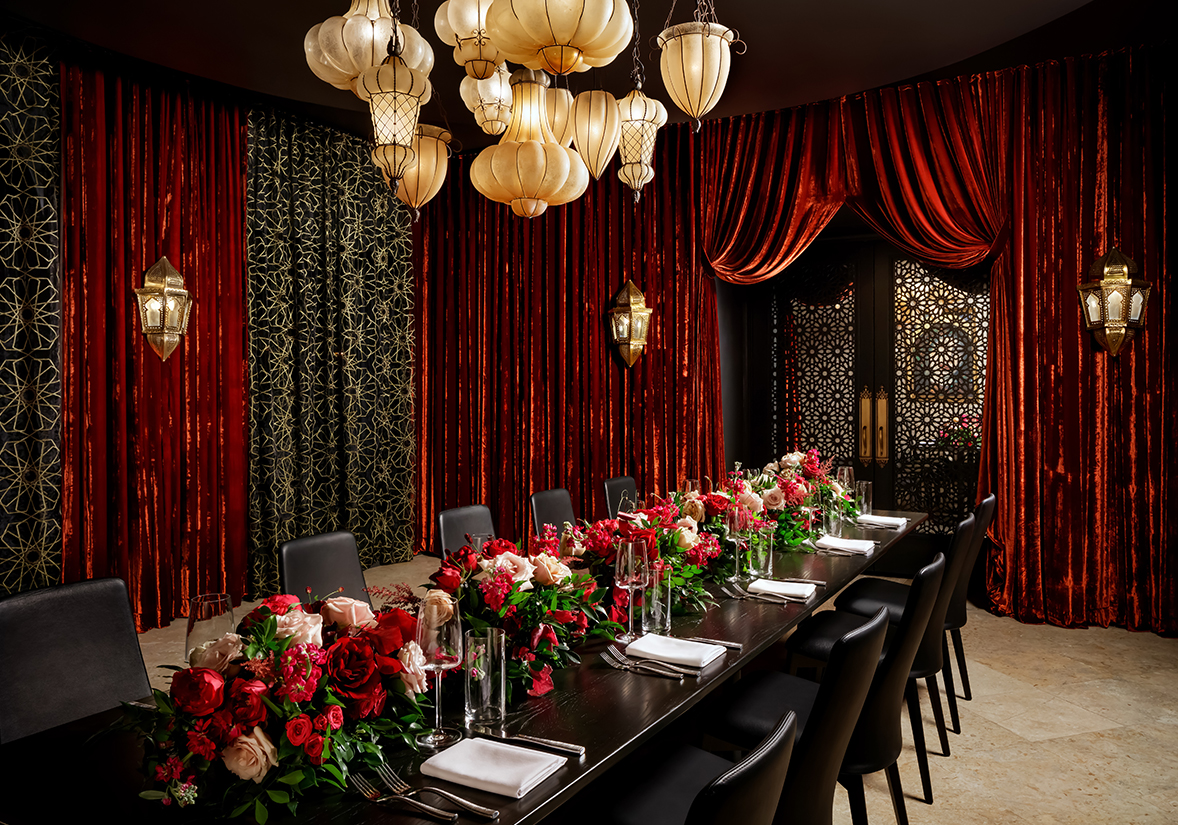 a long table with flowers and chairs in a room with red curtains