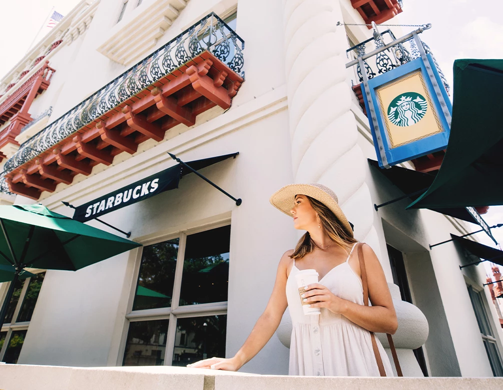 a woman in a white dress and hat holding a coffee cup