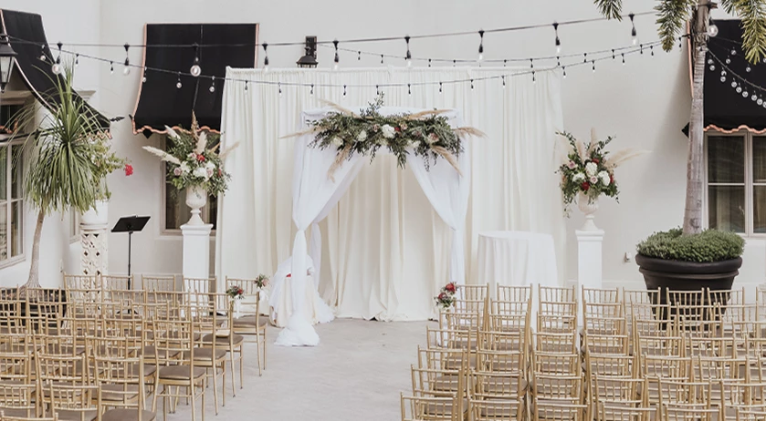 a wedding ceremony with chairs and a white cloth arch