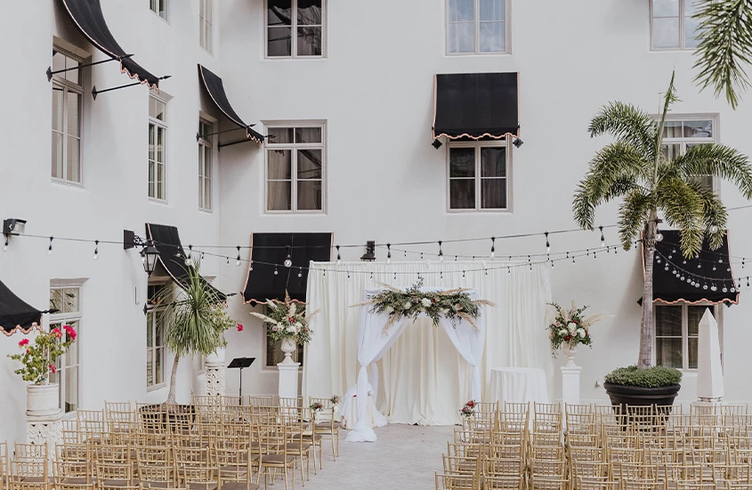 a white building with chairs and a white cloth with a white curtain and flowers