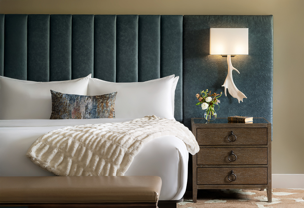 a bed with a white blanket and a lamp on the wall