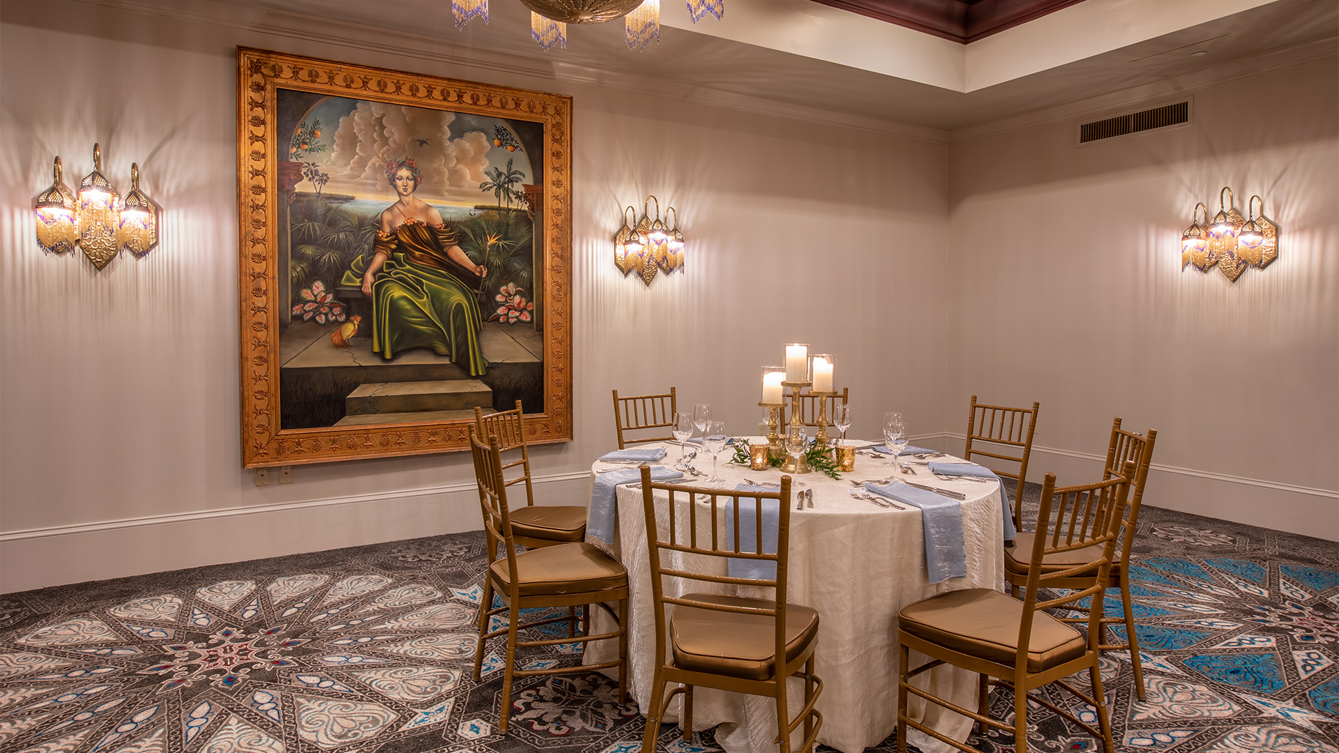 a table set for dinner with candles and a painting on the wall