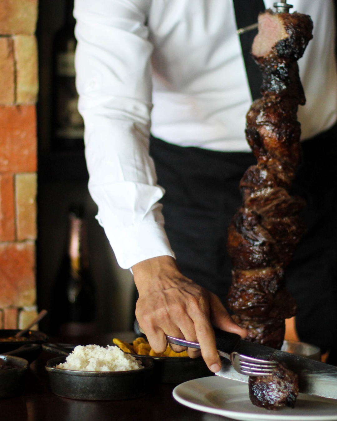 a person holding a fork and knife over a skewer of meat