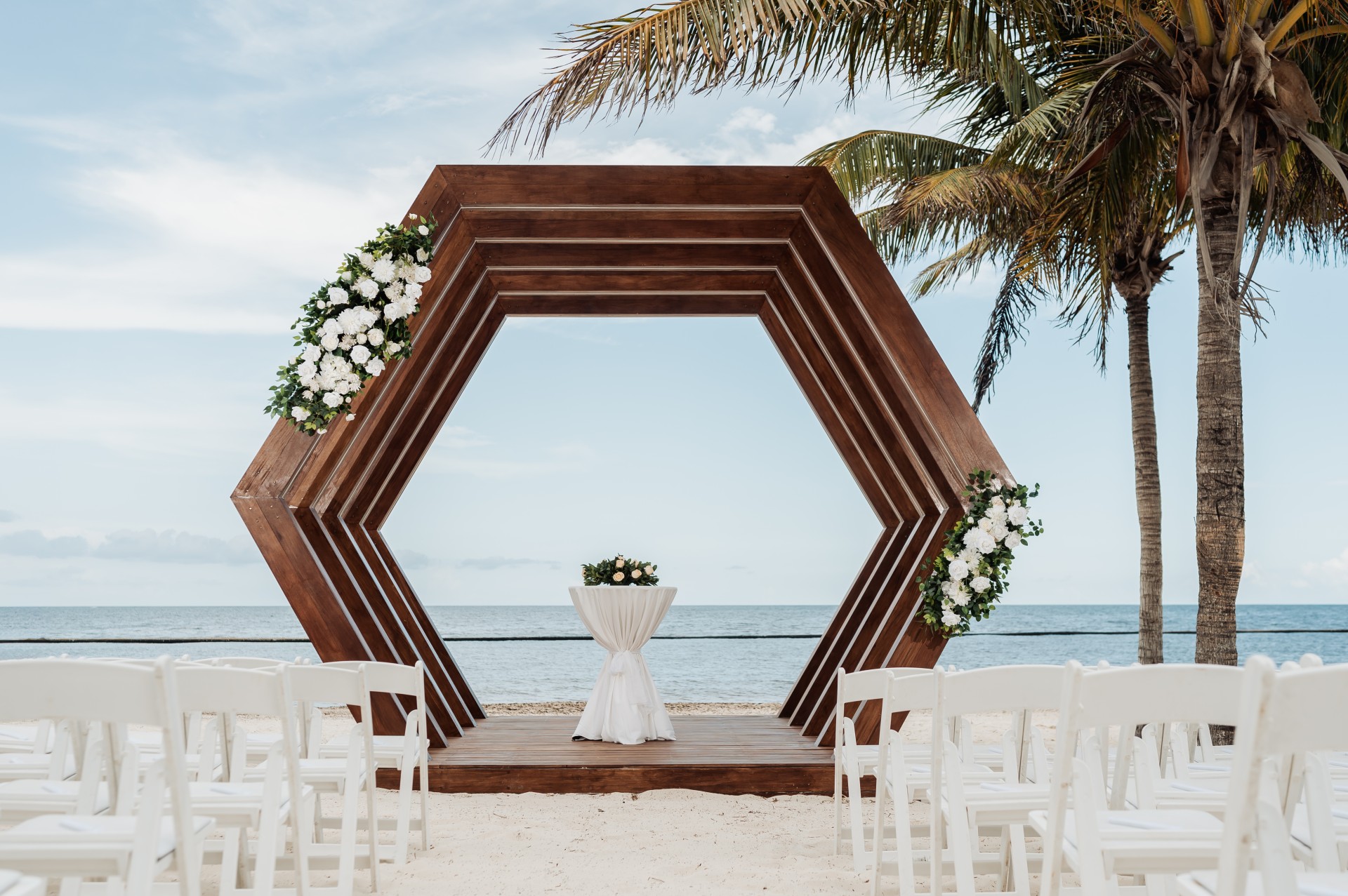 a wooden structure with flowers and chairs on a beach