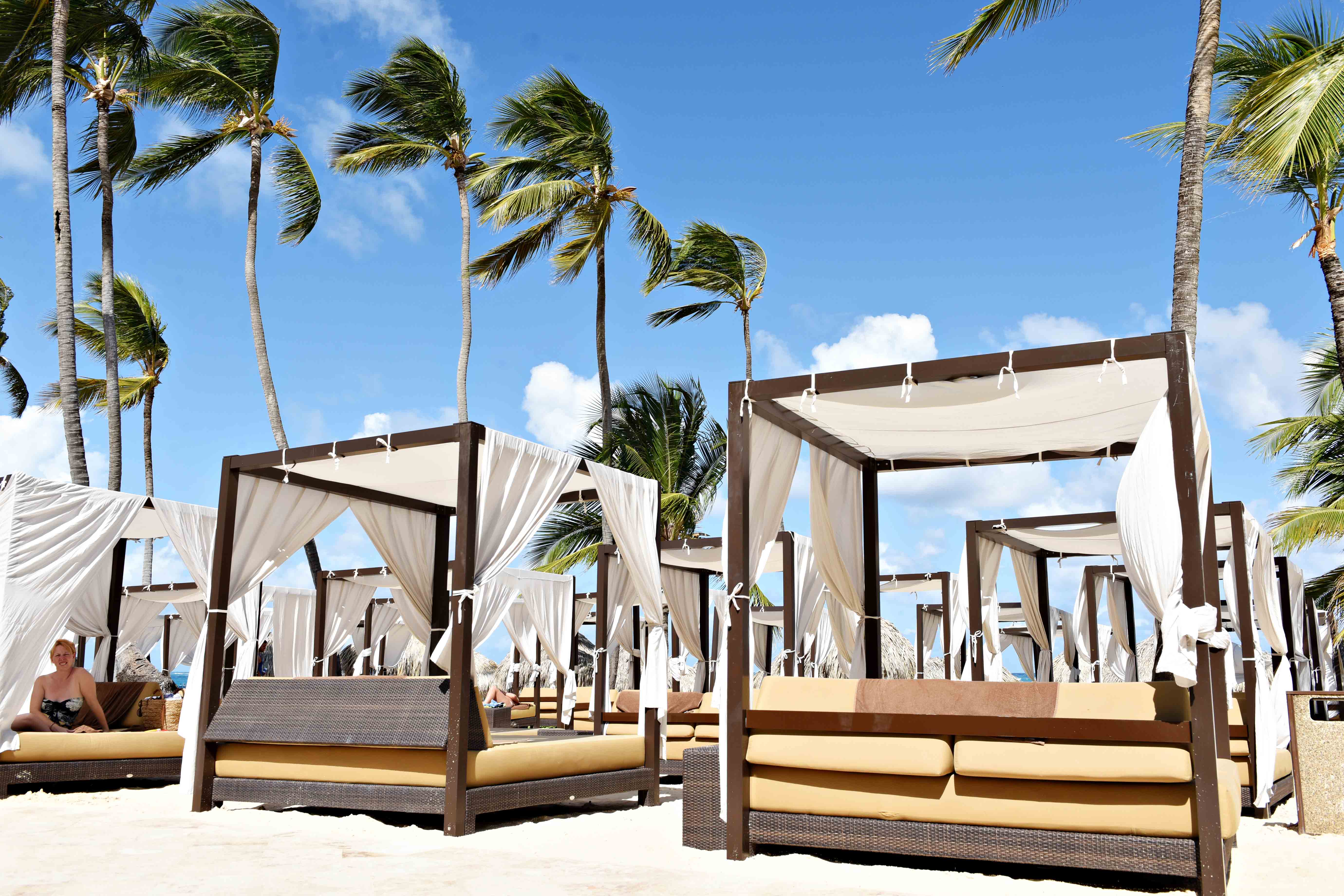 a group of beds with white curtains and a canopy on a beach