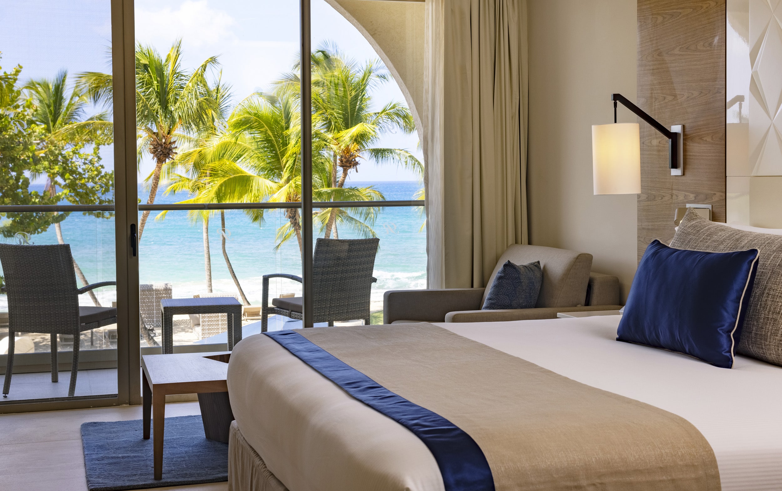 a room with a bed and chairs and a beach view