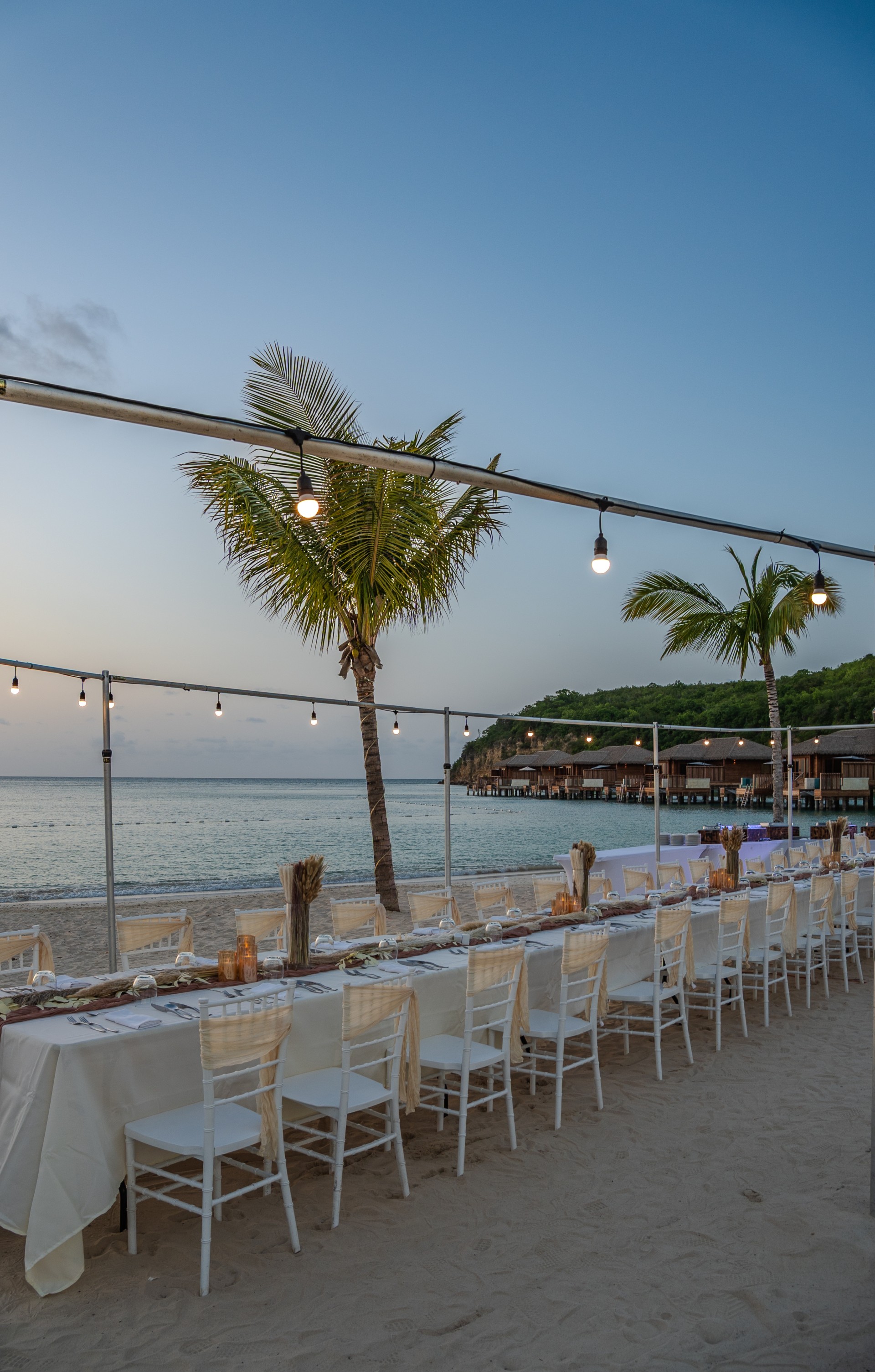 a long table set up on a beach with palm trees and a building in the background