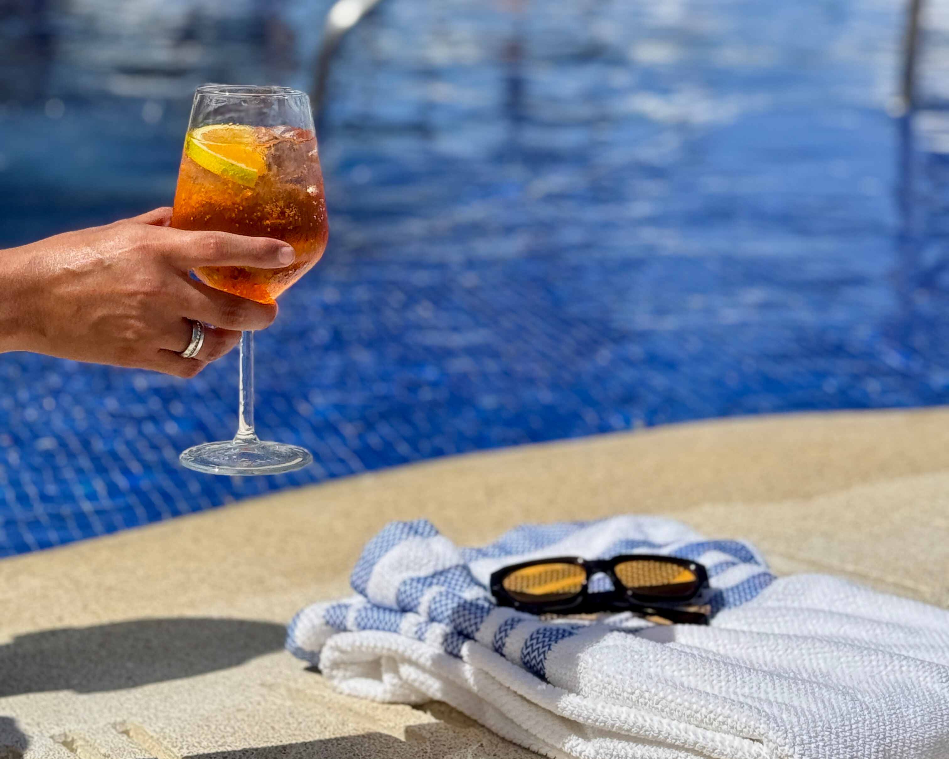 a hand holding a drink next to a towel and sunglasses