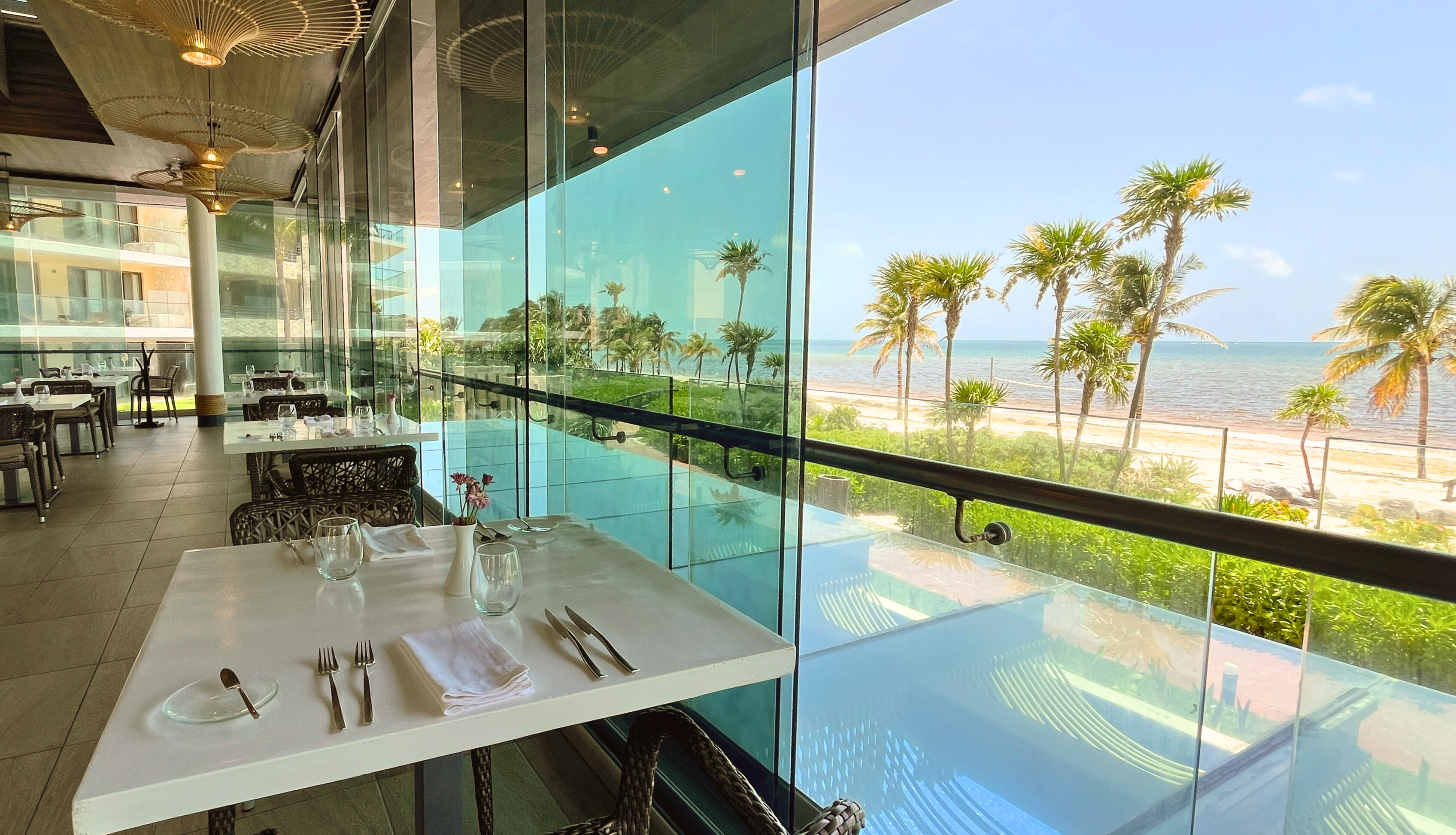 a glass wall with a table and chairs and a beach view
