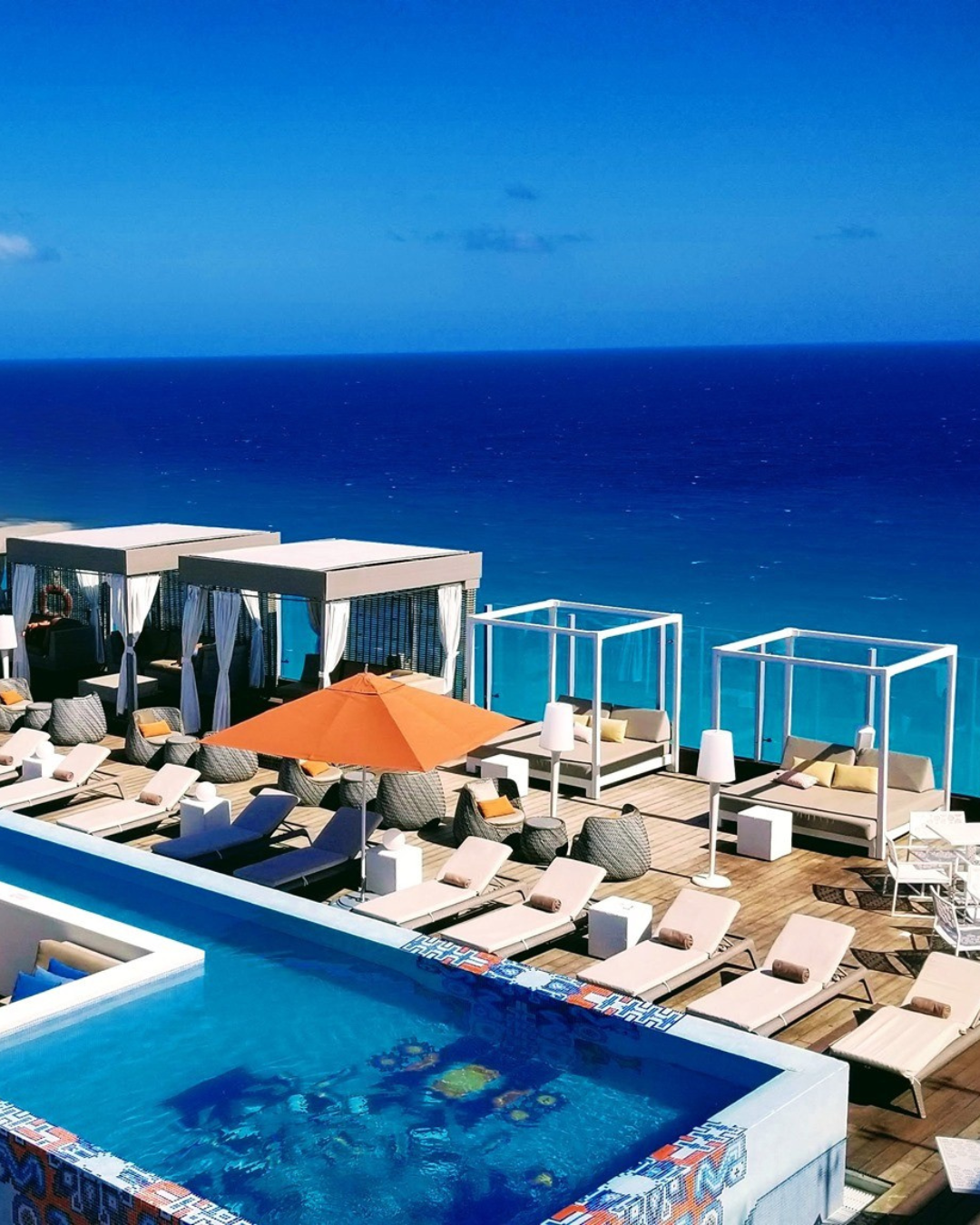 a pool with lounge chairs and umbrellas on a rooftop overlooking the ocean