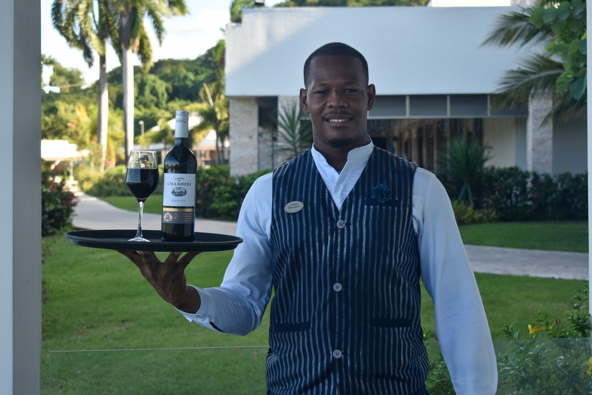 a man holding a tray with a bottle and a glass of wine