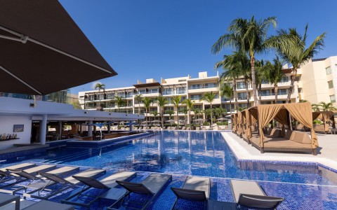 a pool with lounge chairs and palm trees in front of a building
