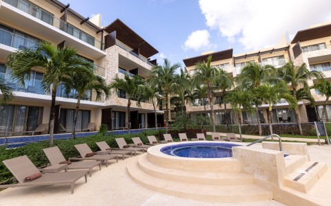 a pool with lounge chairs and palm trees in front of a building