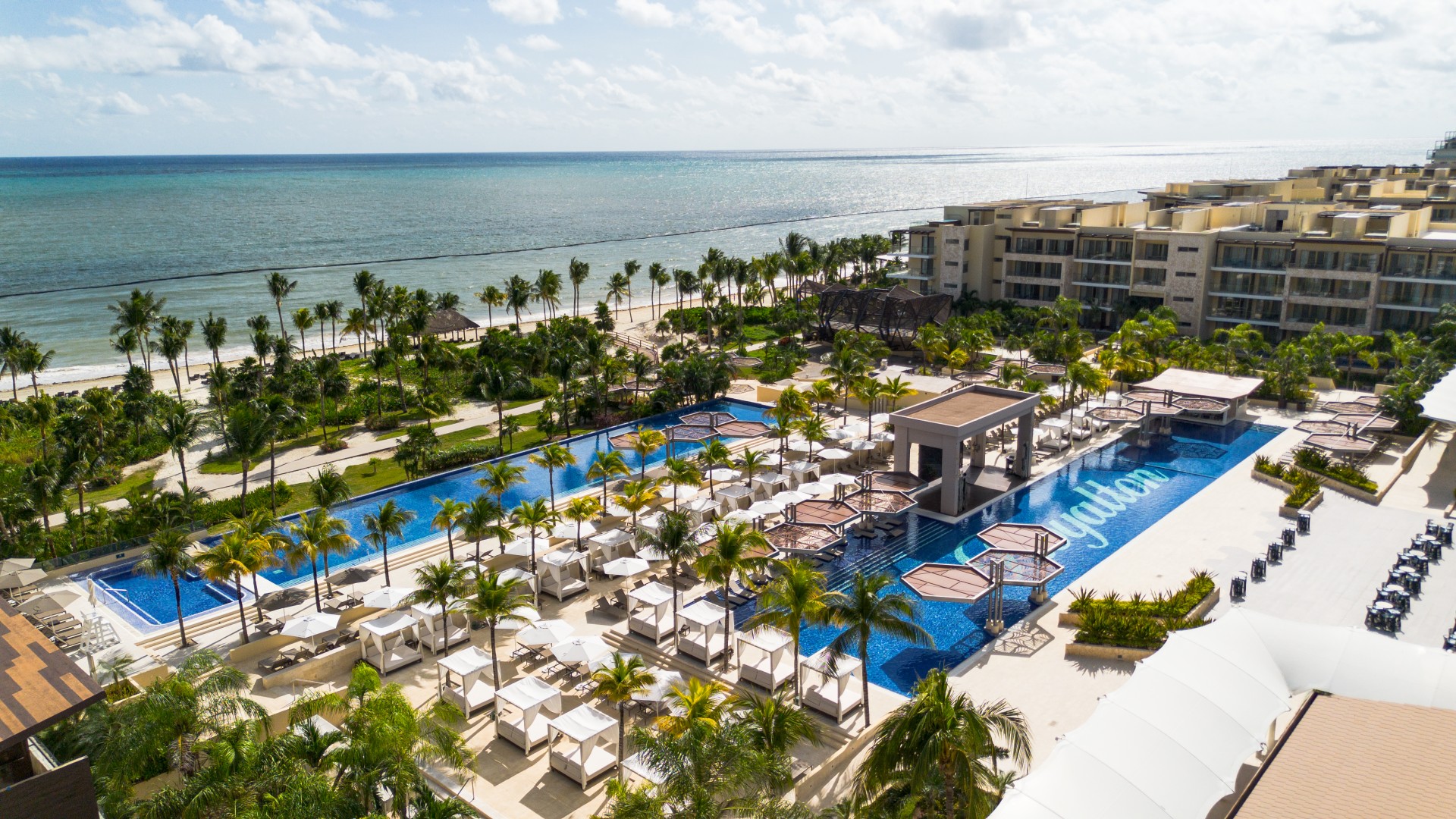 a swimming pool with lounge chairs and palm trees next to a beach