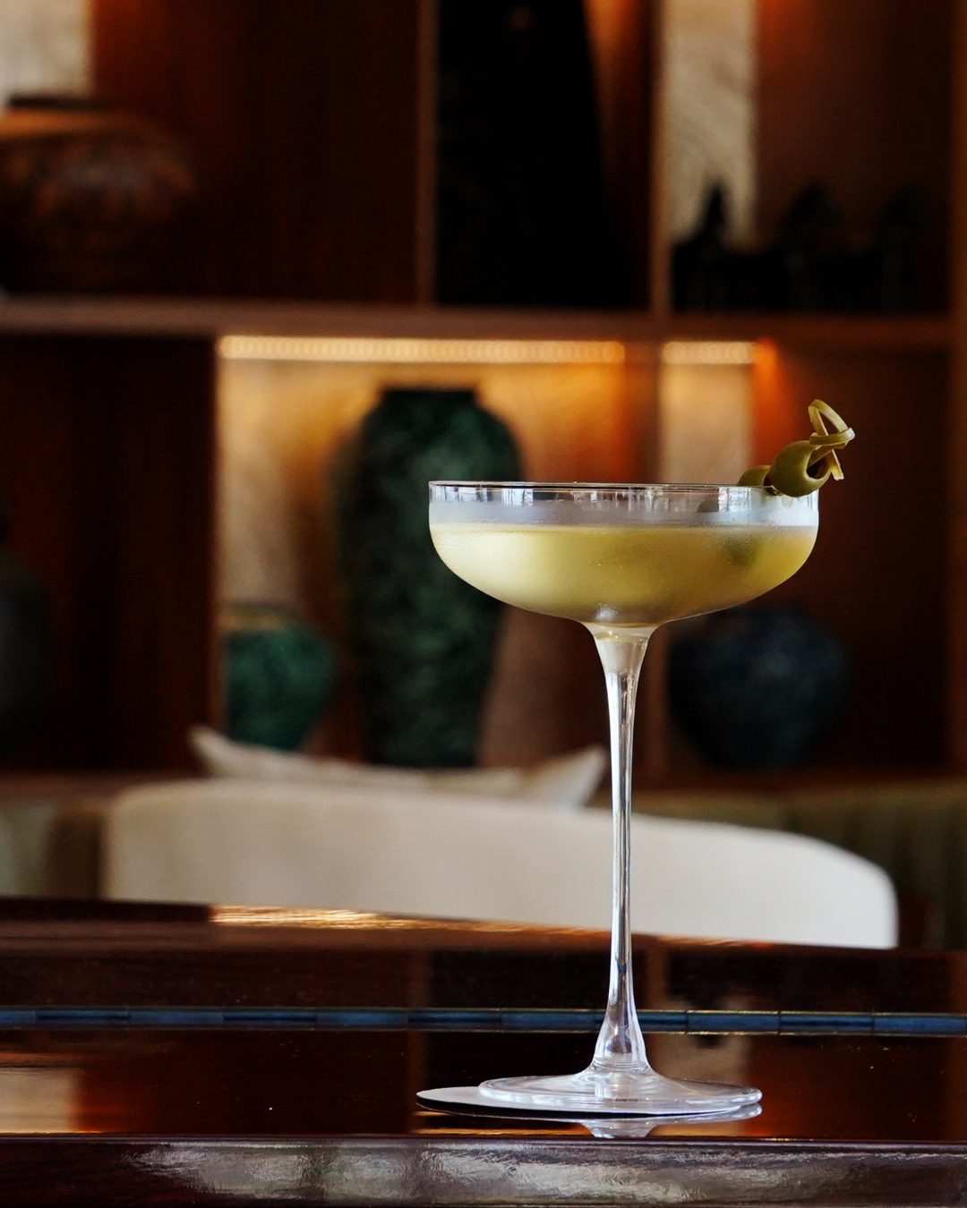 a martini glass with a green olive on top