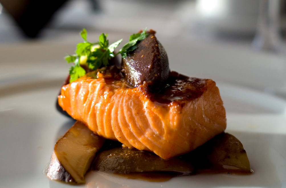 a piece of fish with sauce and vegetables on a white plate