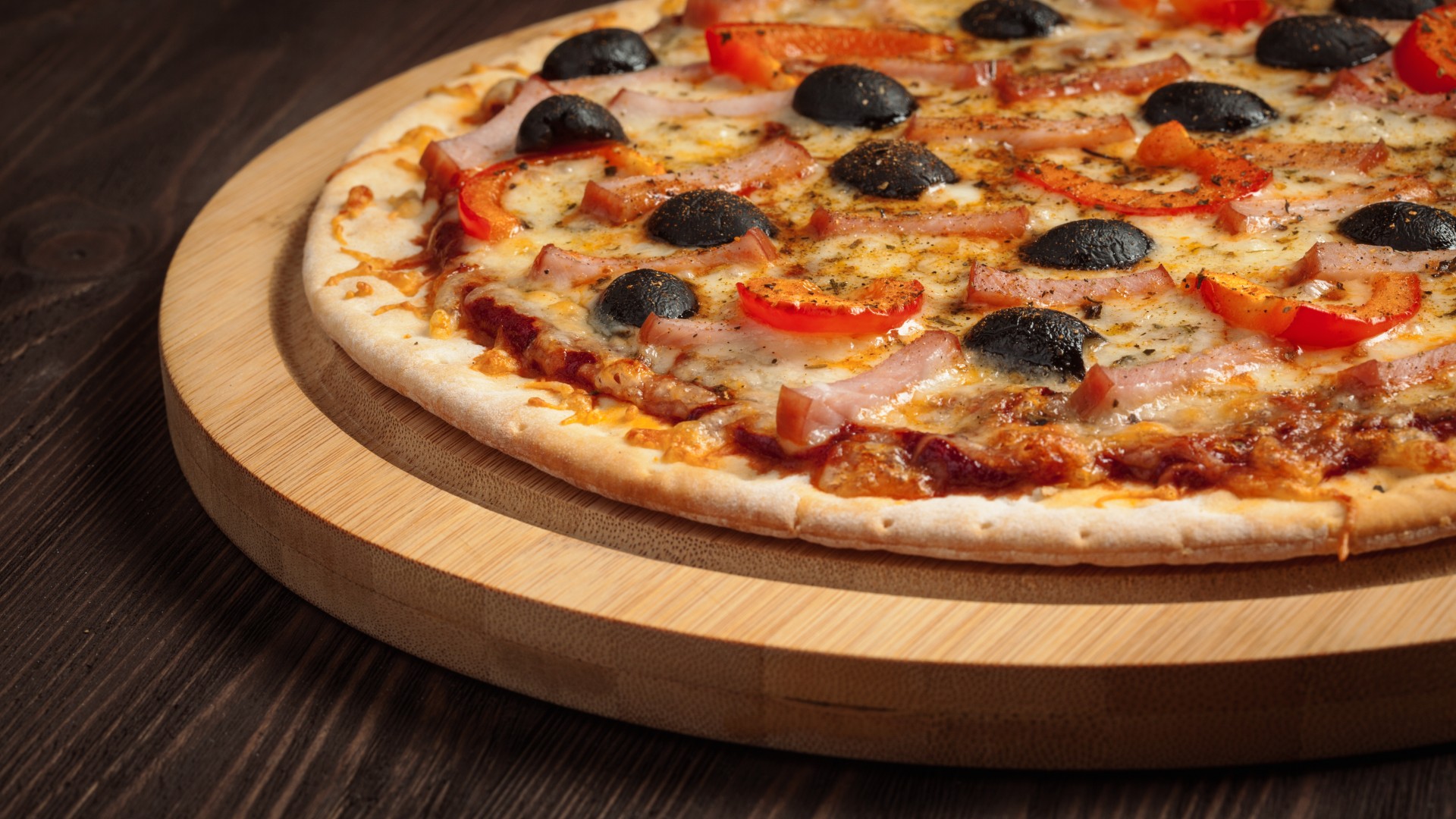 a pizza with olives and ham on a wooden board