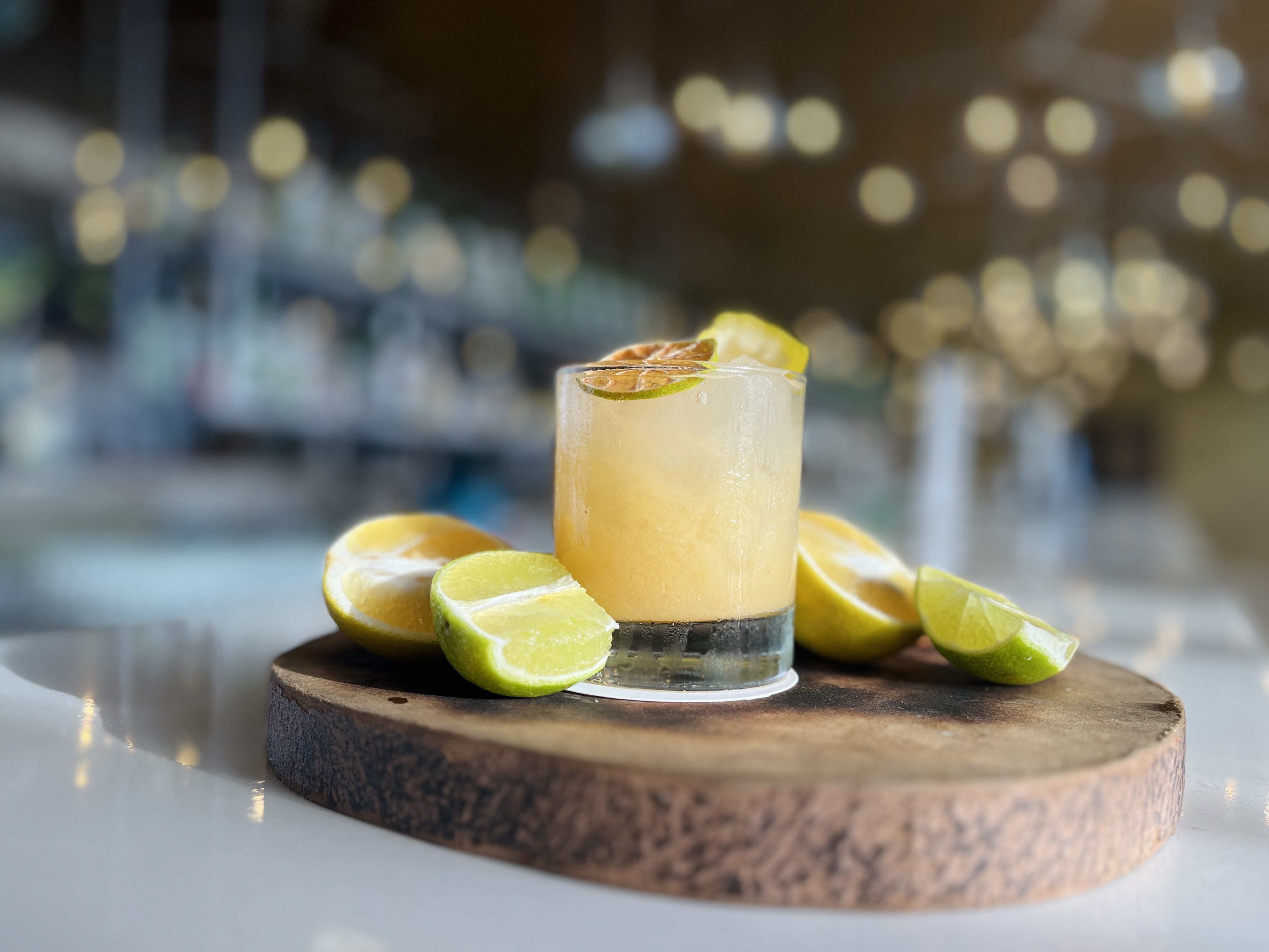 a glass of liquid with a drink and limes on a wooden board