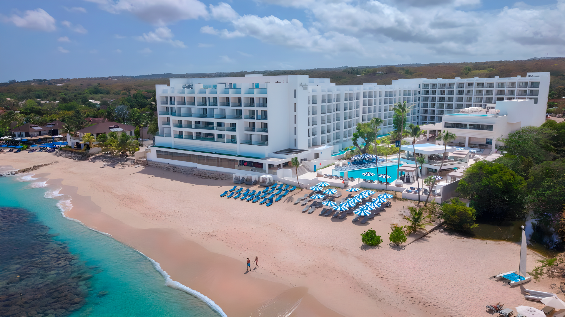 a large white building with blue umbrellas and a beach
