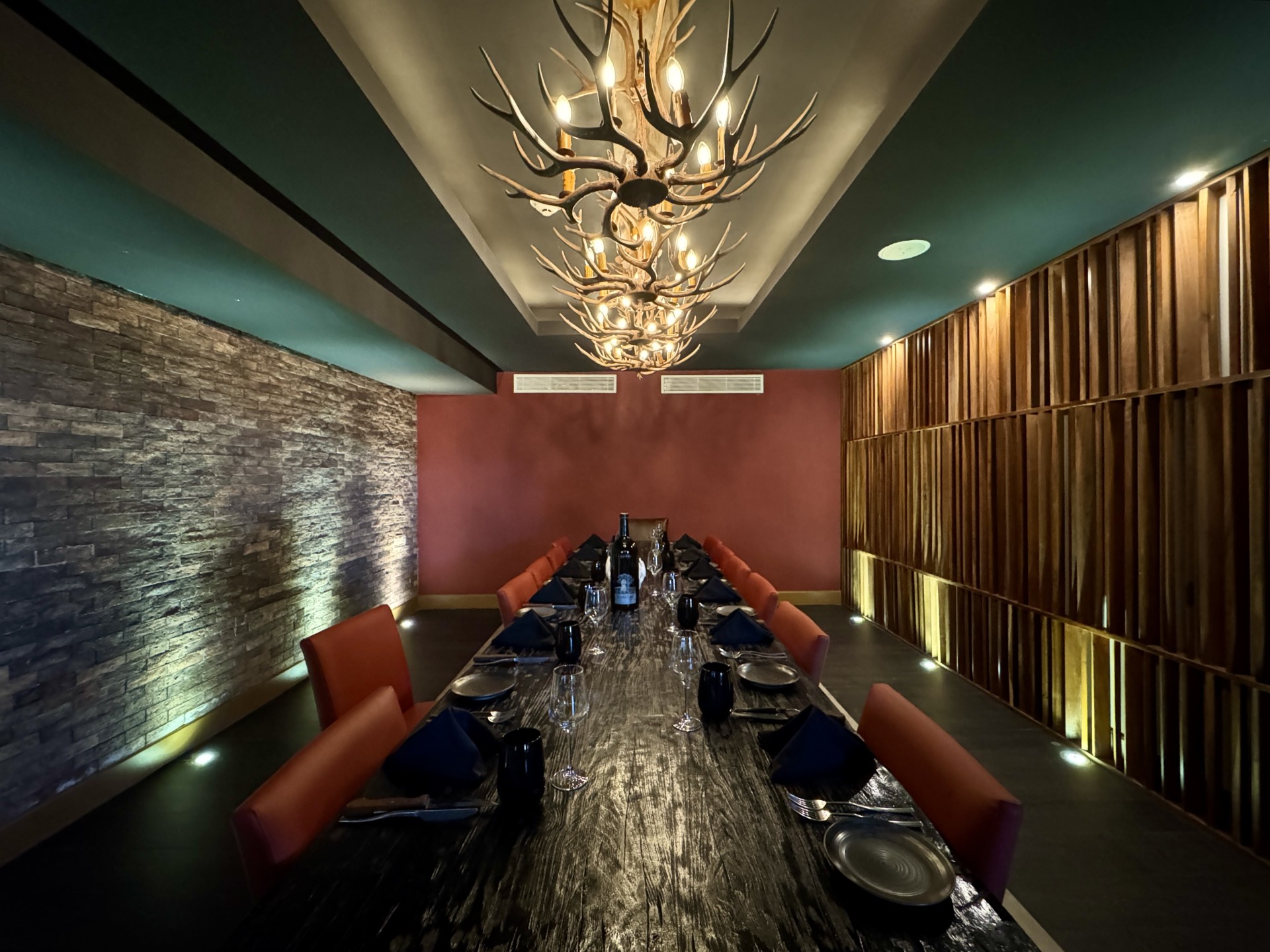 a long table with black plates and red chairs in a room with antlers
