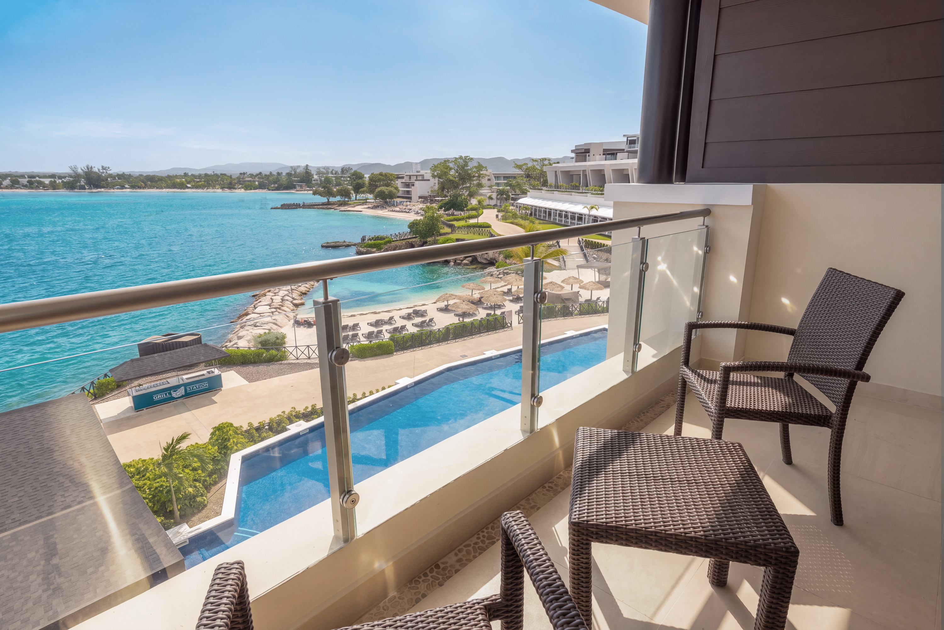 a balcony with chairs and a pool overlooking a beach