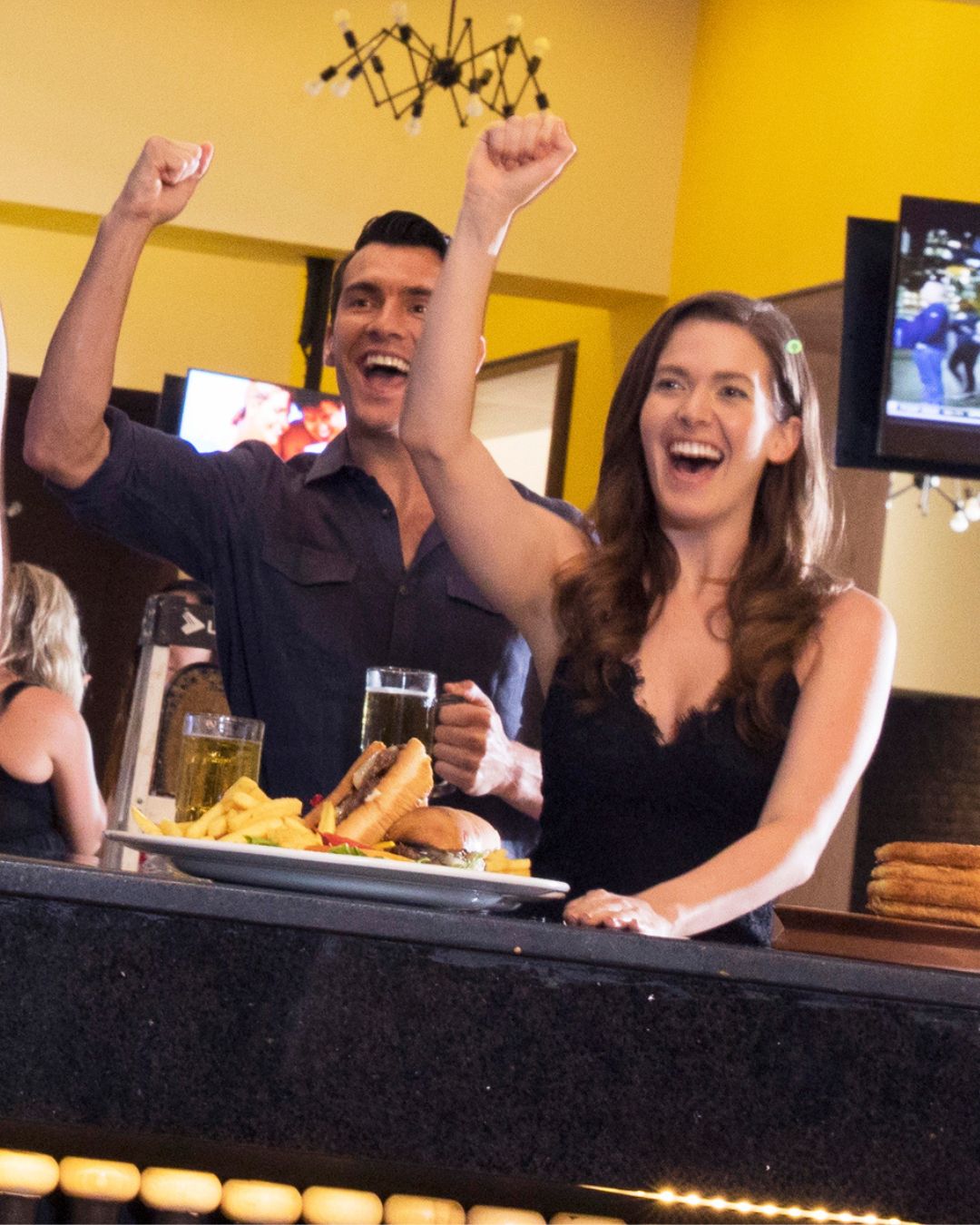 a man and woman with arms up in a bar