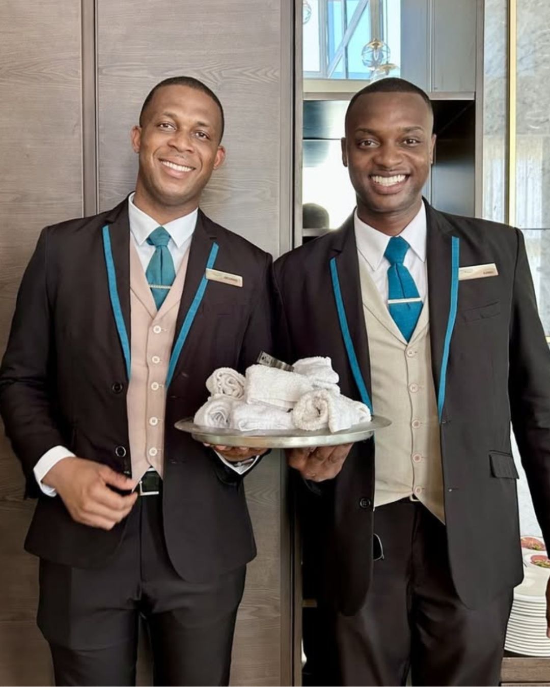 two men wearing suits and ties holding a tray of towels