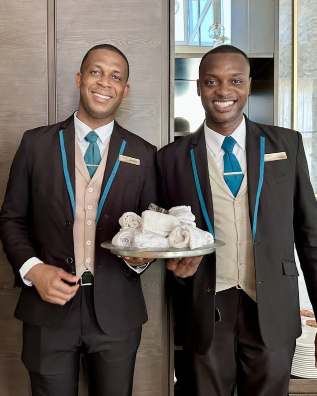 two men wearing suits and ties holding a tray of towels