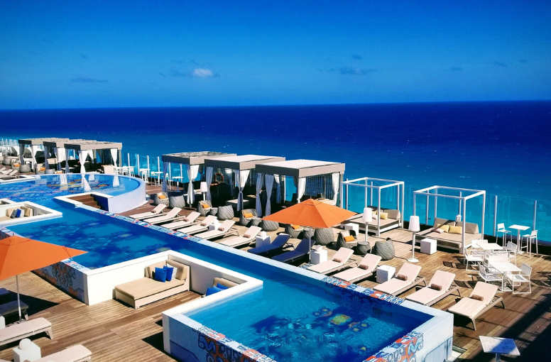 a pool with lounge chairs and umbrellas on a rooftop overlooking the ocean