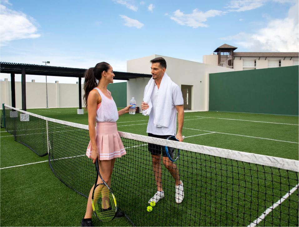 Couple enjoying a friendly tennis match on the courts at Royalton Splash Riviera Cancun, highlighting the resort's sports facilities for guests