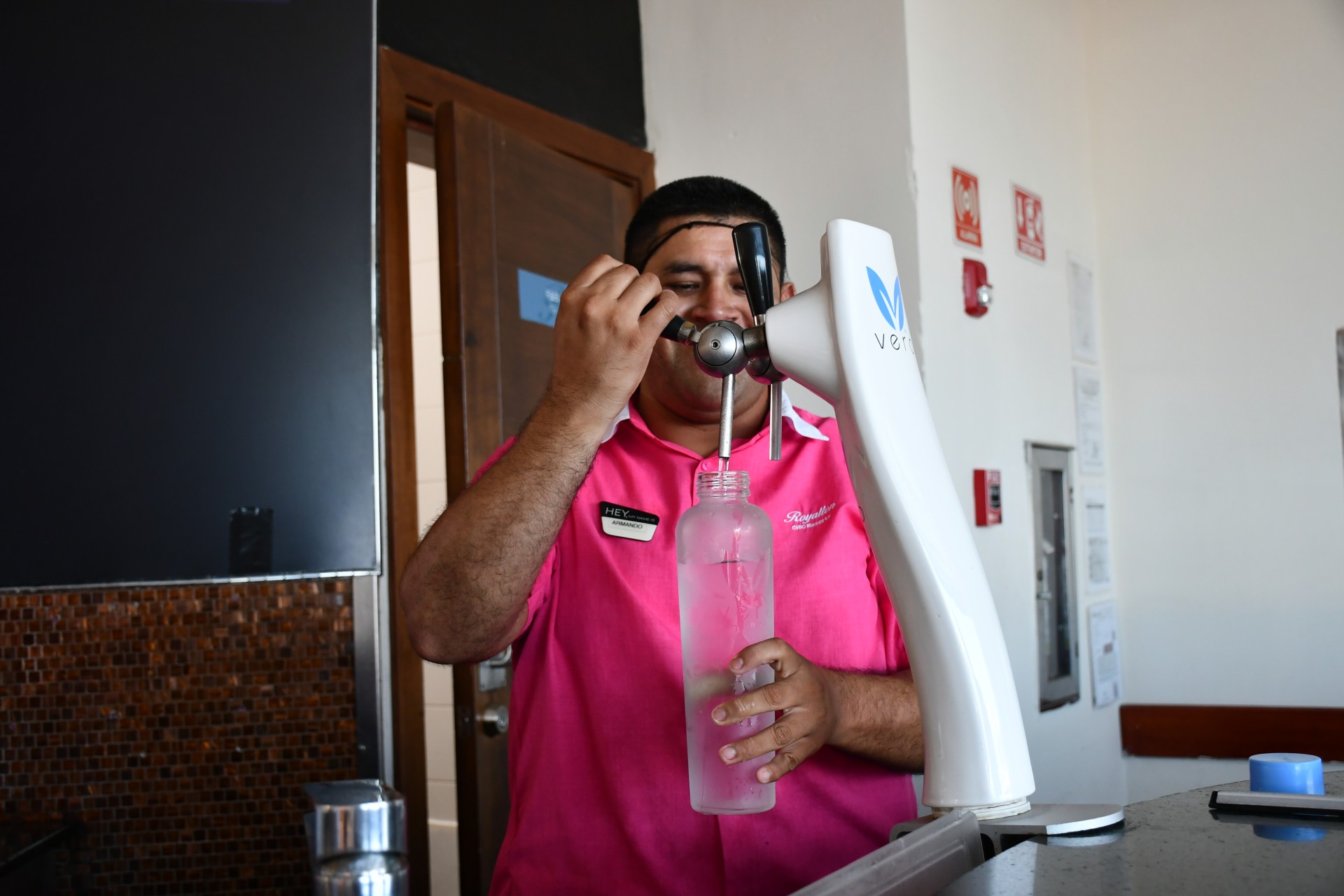 a man in a pink shirt pouring a drink into a bottle