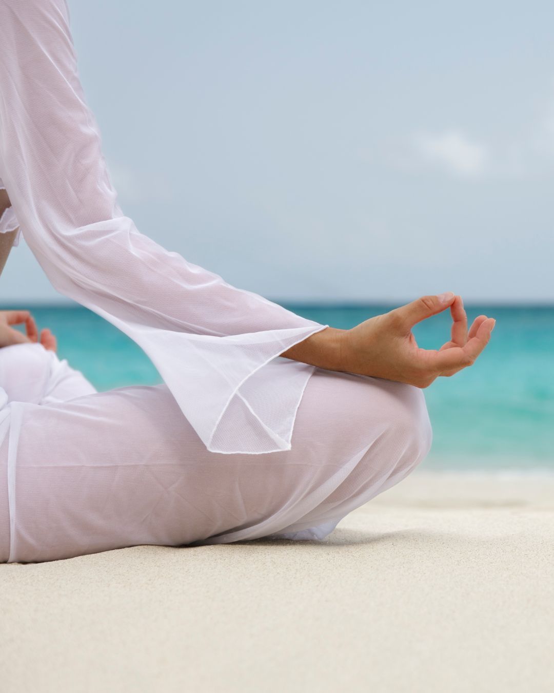 a person in white clothes meditating on a beach