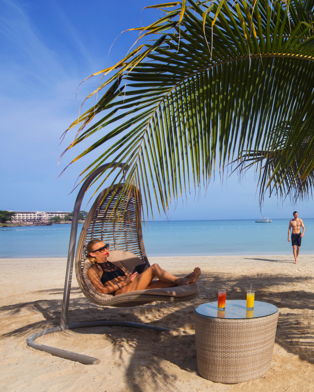 a woman sitting in a chair under a palm tree on a beach