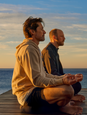 two men sitting on a deck with a body of water in the background