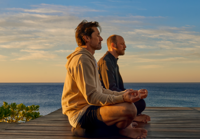 two men sitting on a deck with a body of water in the background
