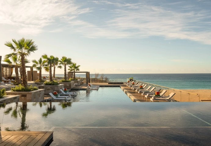 a pool with lounge chairs and a large body of water