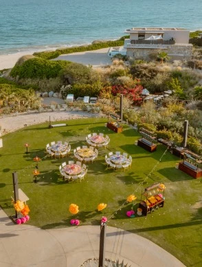 a group of tables and chairs on a lawn with a beach in the background