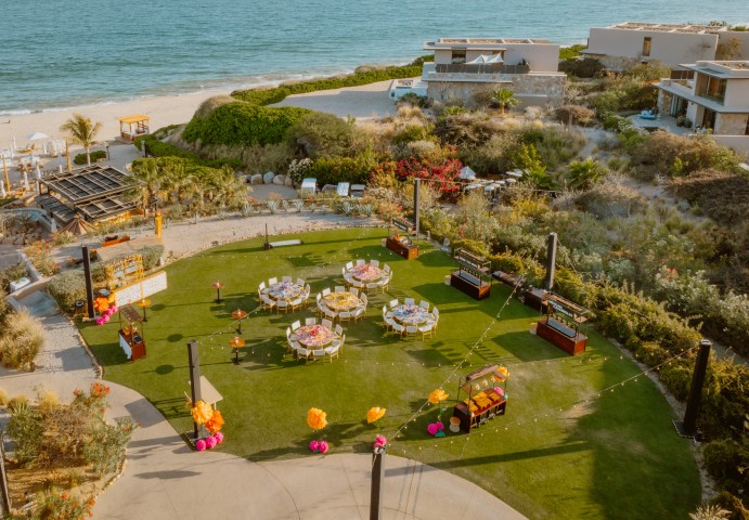 a group of tables and chairs on a lawn with a beach in the background