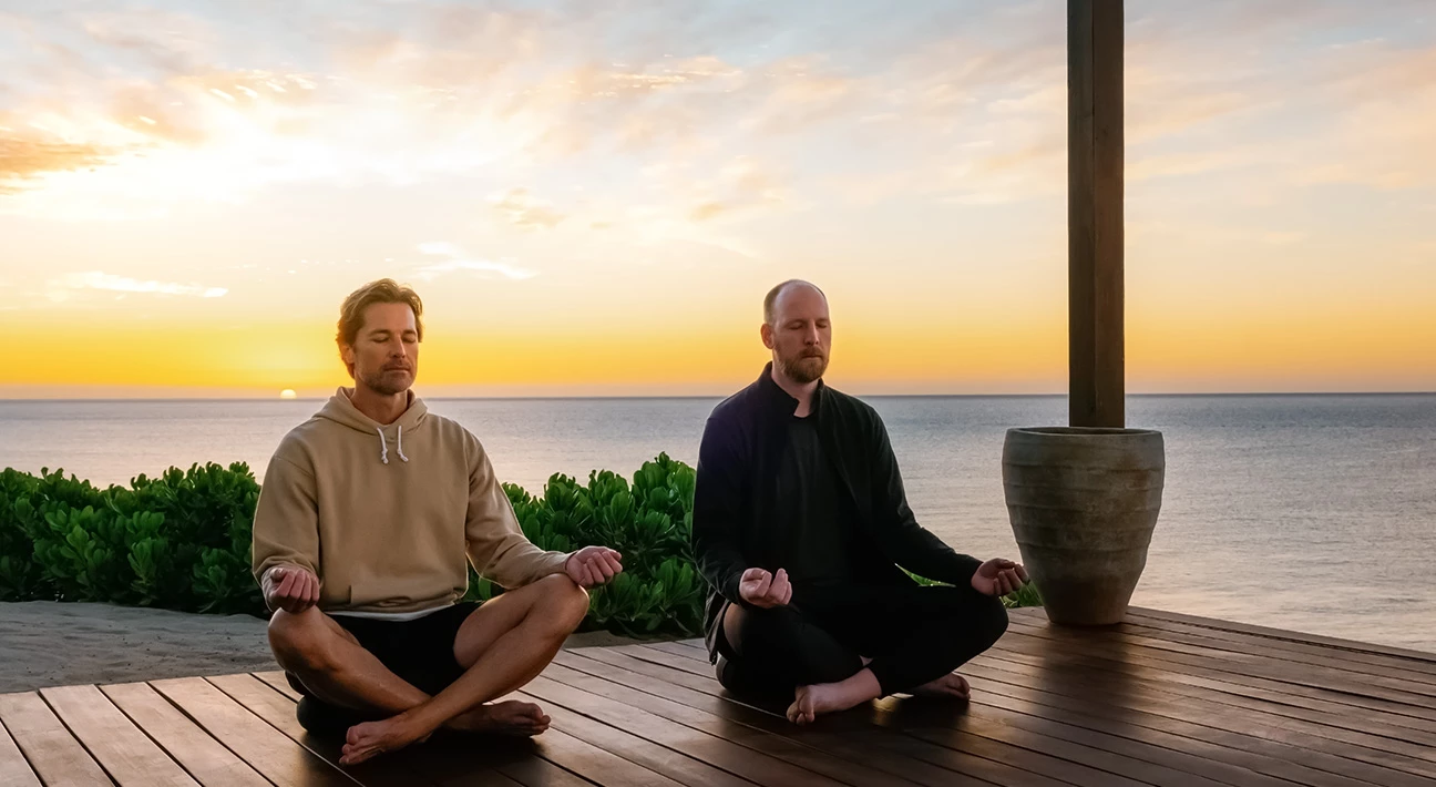 two men sitting on a deck with a pot and water in the background