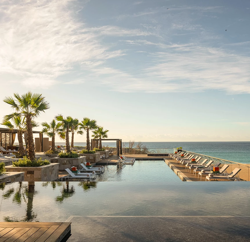 a pool with lounge chairs and palm trees by the ocean