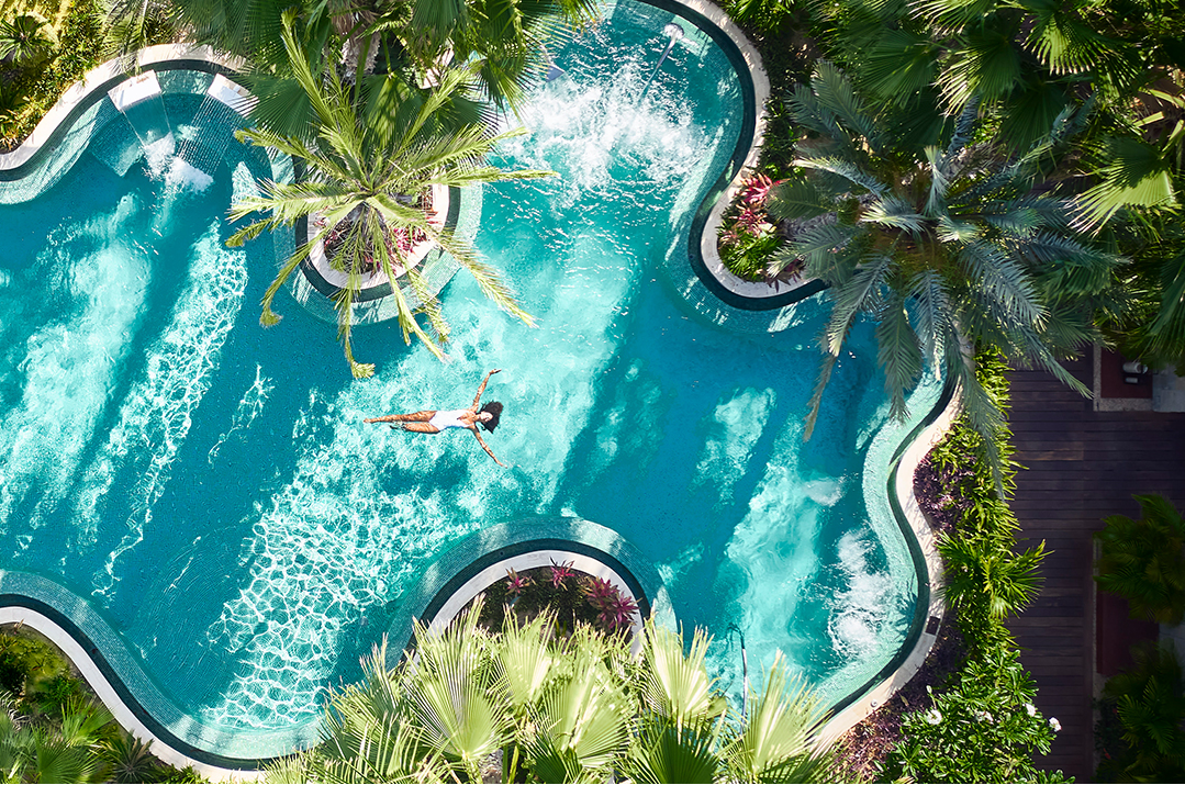a woman in a white swimsuit in a pool surrounded by palm trees