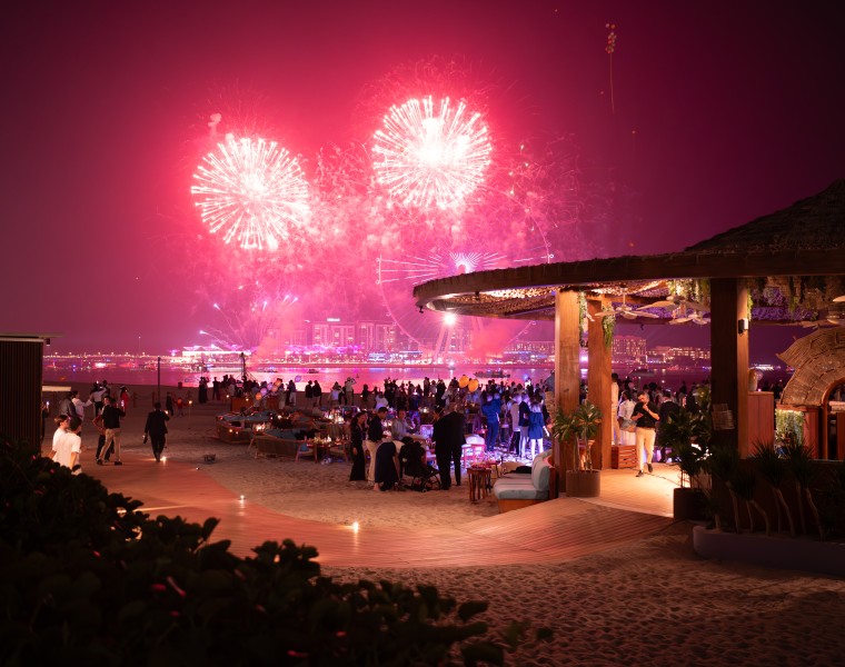 a group of people at a beach with fireworks in the sky