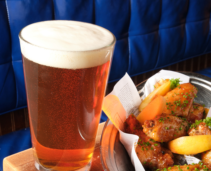 a glass of beer next to a plate of chicken wings