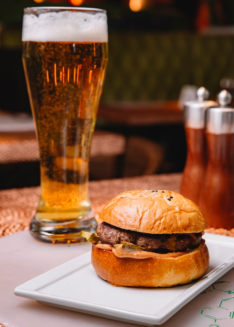 a burger on a plate next to a glass of beer